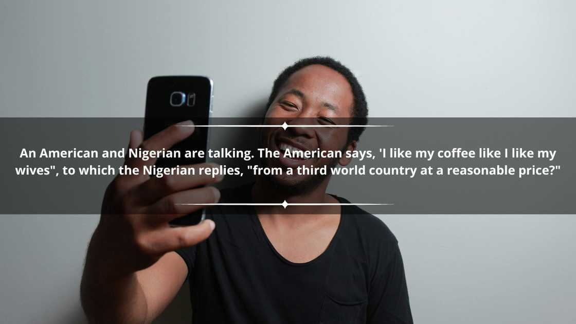 A happy an in a black tee holding a smartphone as he leans against a wall